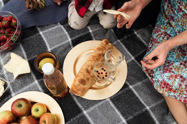 Uma toalha de piquenique está deitada na grama em um dia ensolarado. piquenique para a família. alimentos e bebidas para o almoço estão no cobertor. decoração para um piquenique. comida de piquenique