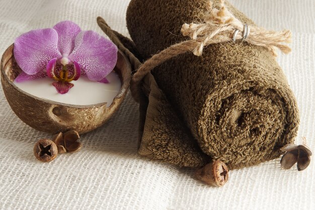 Uma toalha dobrada, amarrada com uma corda e uma flor de orquídea no leite em um coco em um guardanapo de tecido leve, preparação para o procedimento de spa.