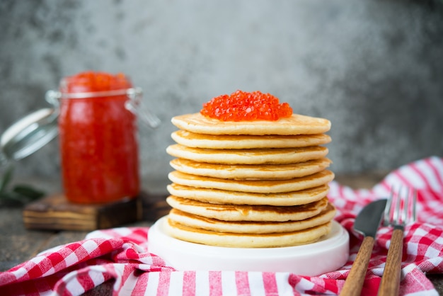 Uma torre de panqueca americana com caviar vermelho fica sobre um fundo cinza de madeira. Foto horizontal.