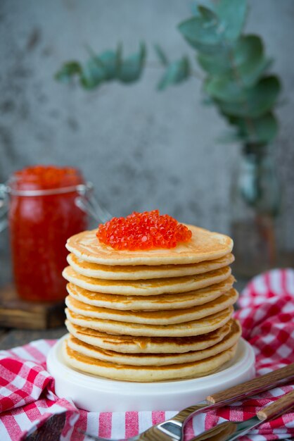 Uma torre de panqueca americana com caviar vermelho fica sobre um fundo cinza de madeira. Foto vertical.