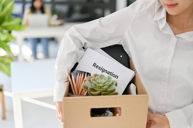 Uma trabalhadora de escritório asiática carregando uma caixa de papelão com suas coisas e carta de demissão