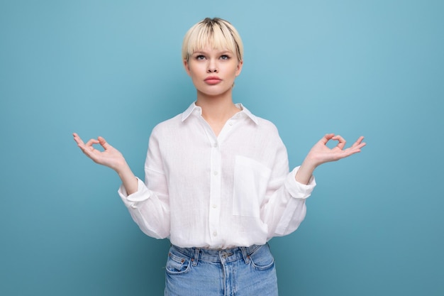 Uma trabalhadora de escritório loira e calma, de camisa branca e jeans, está meditando