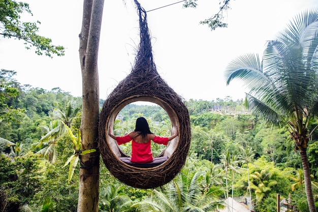 Uma turista feminina está sentada em um grande ninho de pássaro em uma árvore na ilha de Bali