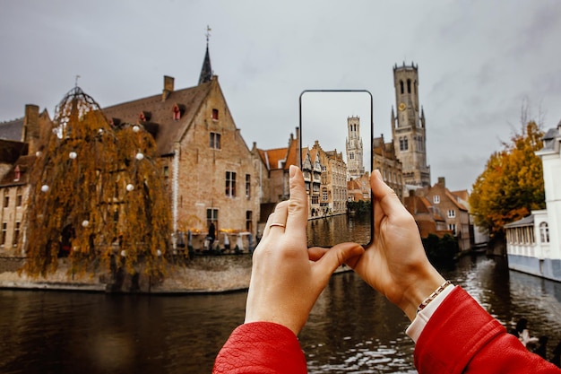 Uma turista fotografa edifícios históricos e um canal em Bruges, Bélgica, usando seu celular