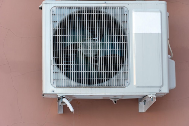 Uma unidade de ar condicionado externa instalada na parede externa de um edifício residencial O ventilador e a grade do radiador do ar condicionado estão próximos