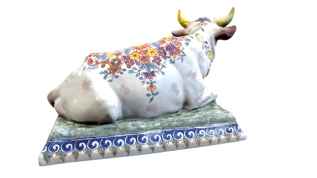 Uma vaca de cerâmica com flores está sentada em um pedestal.