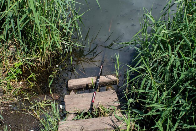 Uma vara de pescar está em uma rampa de madeira ao lado de um corpo d'água.