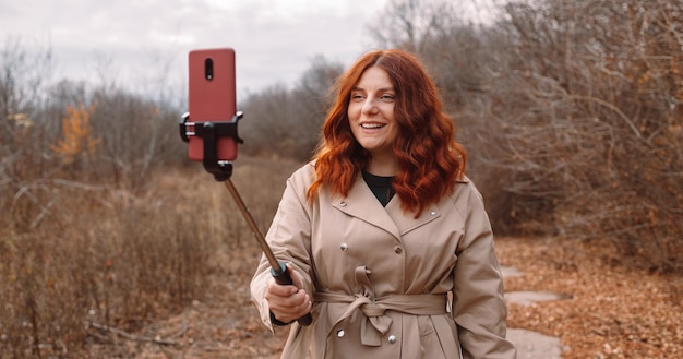 Uma vara de selfie na mão tira uma foto ao ar livre. Jovem alegre tirando foto de selfie no outono outono parque