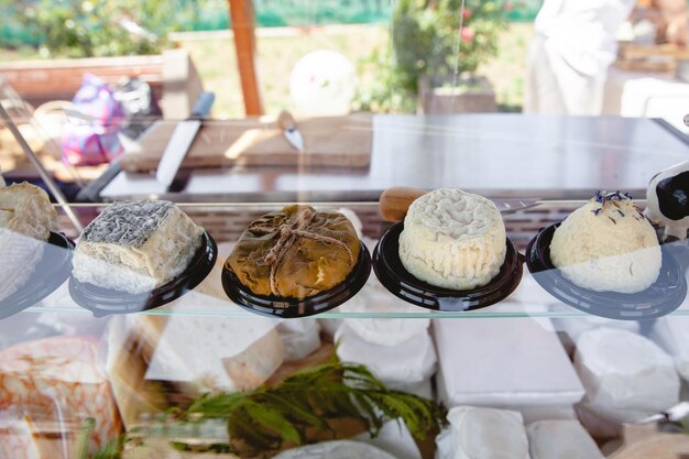 Uma variedade de diferentes tipos de queijo caseiro em uma prateleira de vidro em uma vitrine em uma feira de rua