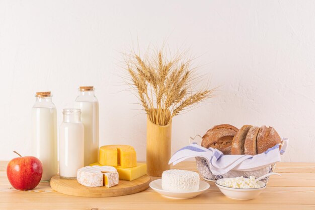 Uma variedade de produtos lácteos frescos pão orelhas de maçã maçãs em uma mesa de madeira guloseimas e símbolos do feriado judaico de Shavuot