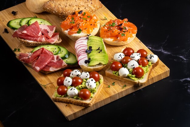 Uma variedade de sanduíches com peixe, queijo, carne e vegetais na mesa e um pão