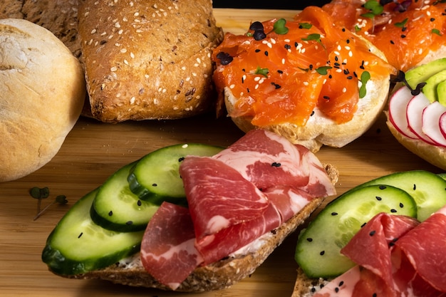Uma variedade de sanduíches com peixe, queijo, carne e vegetais na mesa e um pão