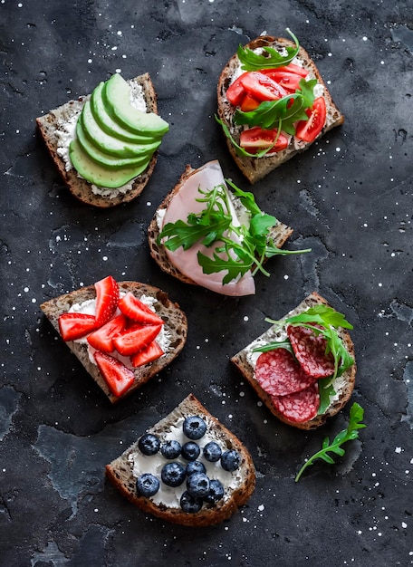 Uma variedade de sanduíches de lanche de tapas de café da manhã em um fundo escuro com queijo creme de abacate bagas de presunto salame tomate cereja