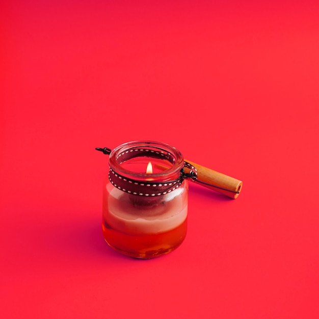 Uma vela queimando em uma jarra como decoração de Natal em fundo vermelho