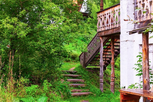 Uma velha escada de madeira em uma floresta entre árvores verdes perto de uma casa vintage e a entrada para o segundo andar