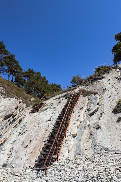 Uma velha escada de metal e enormes pedras brancas em uma praia selvagem.