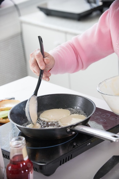 Uma velha fritando panquecas na cozinha colocou a massa na panela