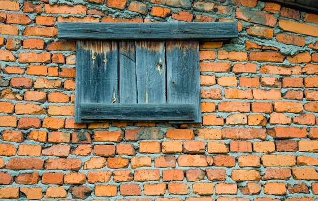 Uma velha janela fechada com tábuas em uma parede de tijolos.
