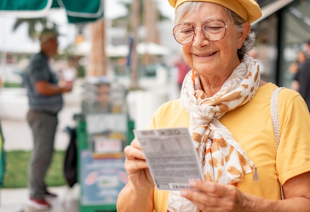 Uma velha sorridente verifica se o bilhete de loteria deu sorte Uma senhora moderna e atraente de amarelo tenta a sorte