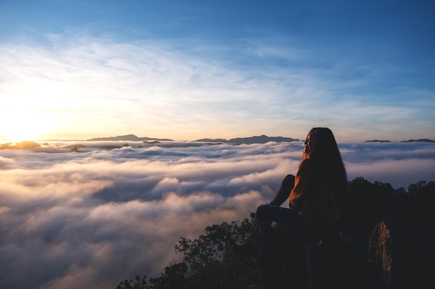 Uma viajante feminina sentada no pico da montanha assistindo o nascer do sol e o mar de neblina