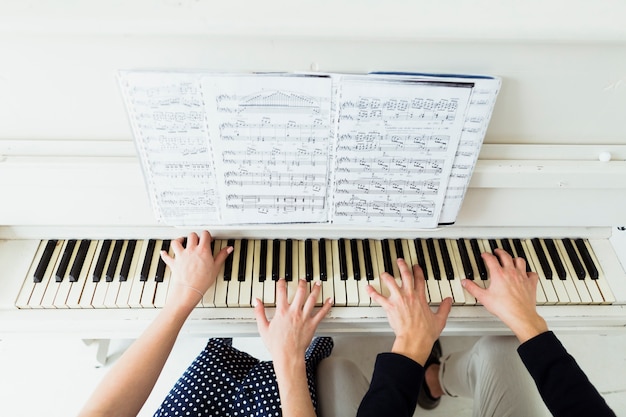 Uma visão aérea da mão do casal tocando piano com folha musical