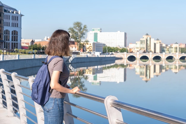 Uma visão traseira de um jovem estudante universitário de cabelos encaracolados em pé em uma área de parque contra o fundo do rio