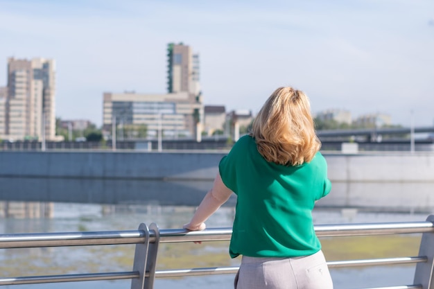 Uma vista da parte de trás de uma garota em uma blusa verde em pé na margem do rio