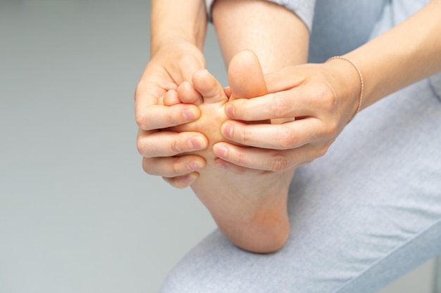 Uma vista de perto de uma mulher caucasiana inspecionando e esfregando os pés separando os dedos dos pés descalços