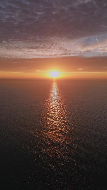 Uma vista de um drone voando sobre o mar no início da manhã ao nascer do sol com o sol nascente e um céu colorido