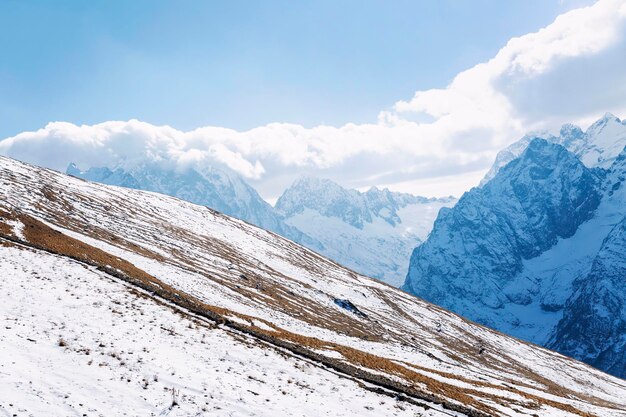 Uma vista magnífica das altas montanhas cobertas de neve em um dia ensolarado, contra o pano de fundo de um céu claro com nuvens. esportes de inverno e atividades ao ar livre. paisagem bonita.