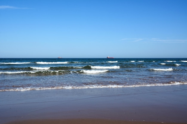Uma vista pitoresca da paisagem marinha da praia Dois navios de carga flutuam no horizonte