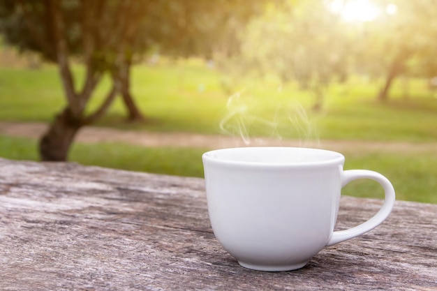 Uma xícara branca de canecas de café expresso quente colocadas em um piso de madeira com neblina matinal e jardim com fundo de luz solar, café da manhã