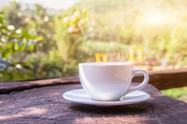 Uma xícara branca de canecas de café expresso quentes colocadas em um piso de madeira com neblina matinal e montanhas