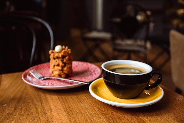 Uma xícara cerâmica de café preto e uma sobremesa servida em um prato na mesa de madeira em um café