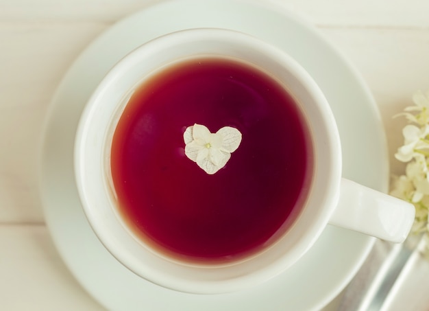 Uma xícara com chá fica em livros sobre um fundo branco. Flores em forma de coração. Café da manhã romântico.