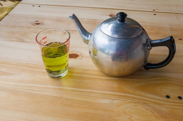 Uma xícara com chá verde e bule no fundo da mesa de madeira branca