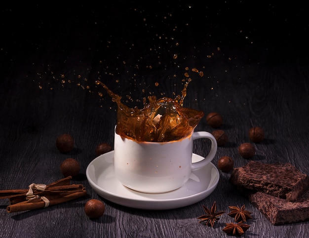 Uma xícara com respingo de café com nozes e pau de canela na madeira da mesa sobre fundo escuro