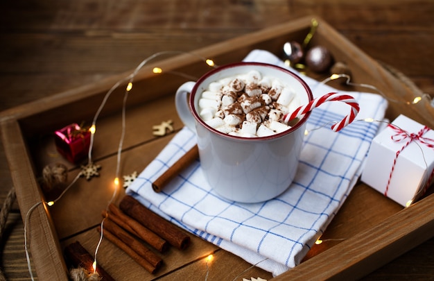 Uma xícara de bebida quente de Natal em um fundo de madeira em torno de um pau de canela e presentes de Natal.