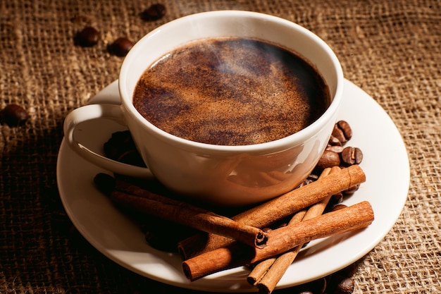 Uma xícara de café acabado de fazer fuma em um prato de paus de canela