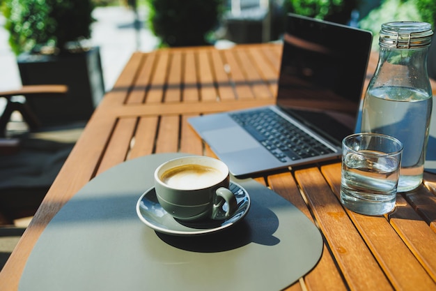 Uma xícara de café aromático no fundo de um laptop em um terraço de verão Trabalhar em um café Trabalho remoto on-line