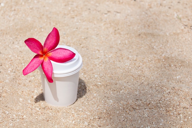 Uma xícara de café branca com flor rosa na areia.