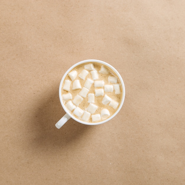 Uma xícara de café branca com marshmallows contra o papel marrom ofício.