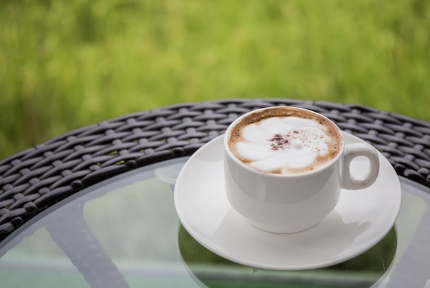 Uma xícara de café branca na mesa com um pano de fundo de campos de arroz