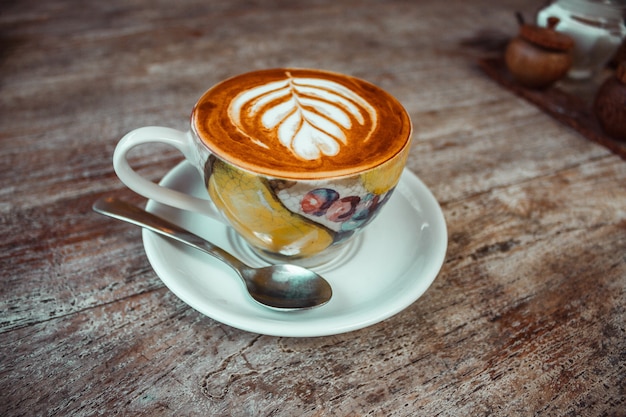 Uma xícara de café cappuccino matinal com padrão de creme, linda caneca colorida e colher na mesa de madeira