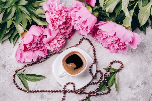 Uma xícara de café com pires e miçangas com flores de peônias rosa