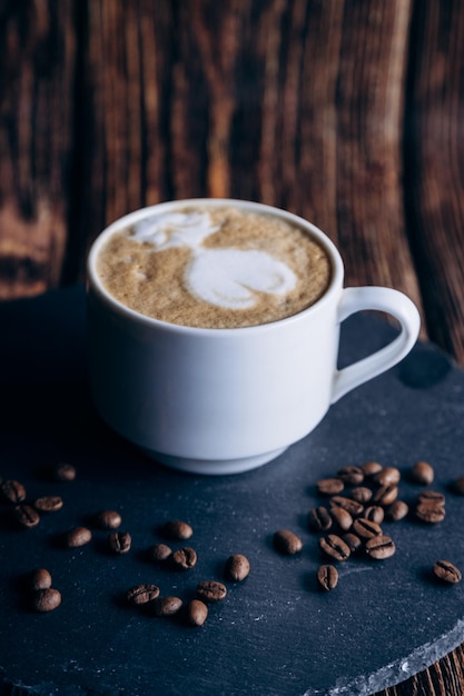 Uma xícara de café com um latte em cima de uma mesa preta com grãos de café.