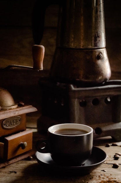 Uma xícara de café com um moedor de café manual e um gêiser sobre uma mesa de madeira.