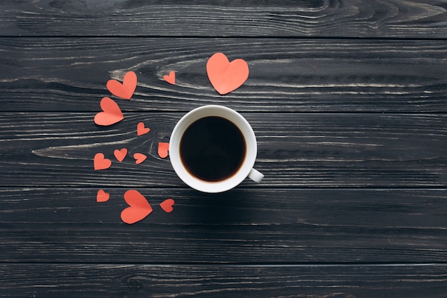 Uma xícara de café e corações de papel decorativo em um fundo de madeira escura no dia dos namorados.