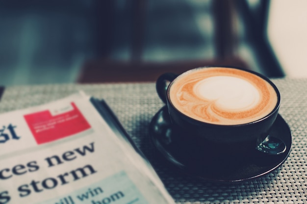 Uma xícara de café e um jornal de café em uma mesa de madeira