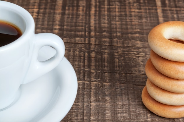 Uma xícara de café e uns bagels cozidos fecham-se acima. Em uma textura de madeira.